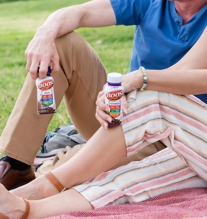 An image showing partial human bodies sitting on the grass drinking boost supplement drink.